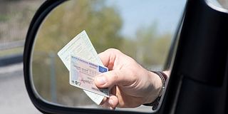 Hand reicht Führerschein und Fahrzeugpapiere aus Autofenster