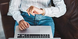 Person mit Laptop schaut auf die Uhr