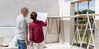 Paar steht mit Bauplan auf der Baustelle