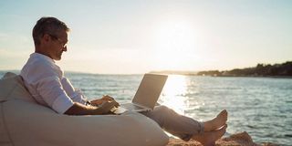 Remote Work Mann arbeitet mit Laptop am Meer