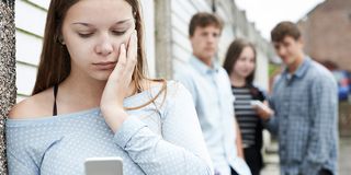 Mädchen schaut traurig auf ihr Handy andere Jugendliche im Hintergrund