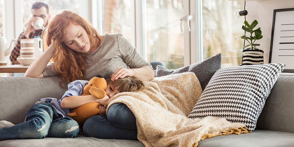 Kind krank – Lohnfortzahlung Mutter mit krankem Kind auf dem Sofa