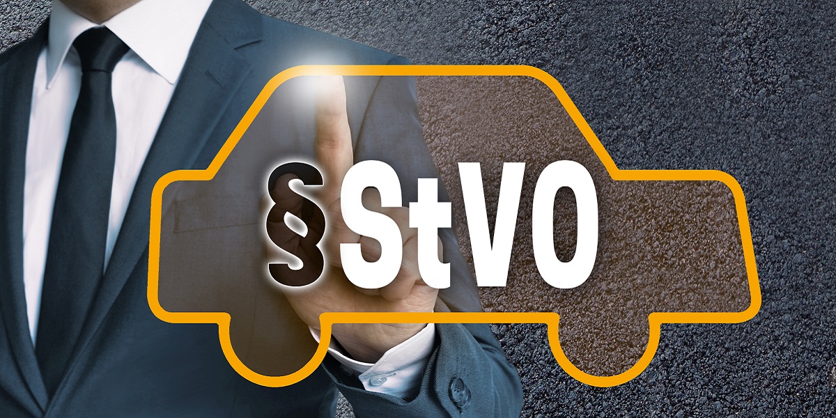 Mann im Anzug zeigt mit dem Finger auf eine grafische Darstellung, auf der die Kontur eines Fahrzeuges und die Buchstaben S t V O hinter einem Paragraphen-Zeichen abgebildet sind